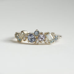 a macro photo of a yellow gold ring with blue gems of various colors sizes and shapes are mixed with round white diamonds on a matte white background