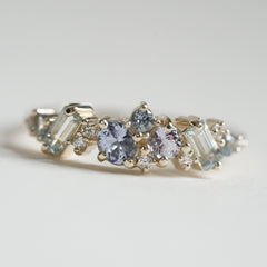 a macro photo of a yellow gold ring with blue gems of various colors sizes and shapes are mixed with round white diamonds on a matte white background