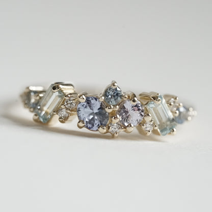 a macro photo of a yellow gold ring with blue gems of various colors sizes and shapes are mixed with round white diamonds on a matte white background