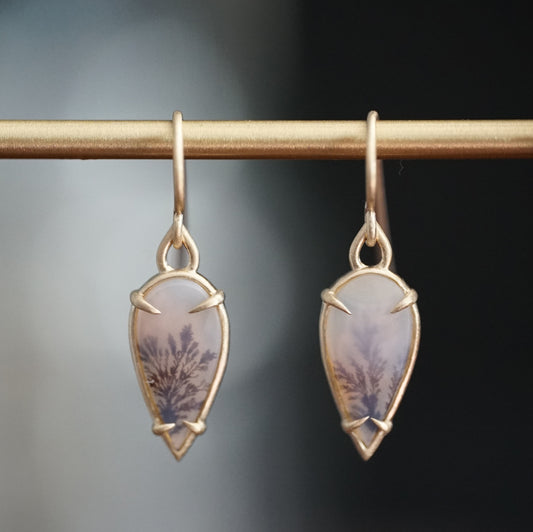 a pair of yellow gold drop earrings with dendritic agates hang on a brass bar