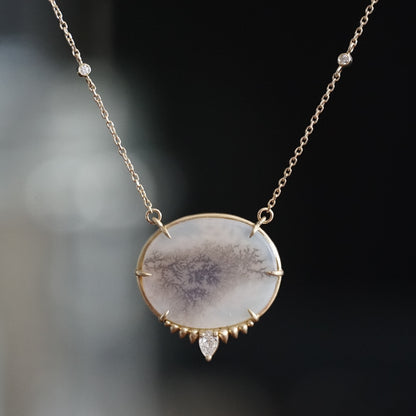 a yellow gold necklace featuring an oval dendritic agate center stone with a pear shape diamond at the base hangs on an open link chain with two bezel set diamond accents