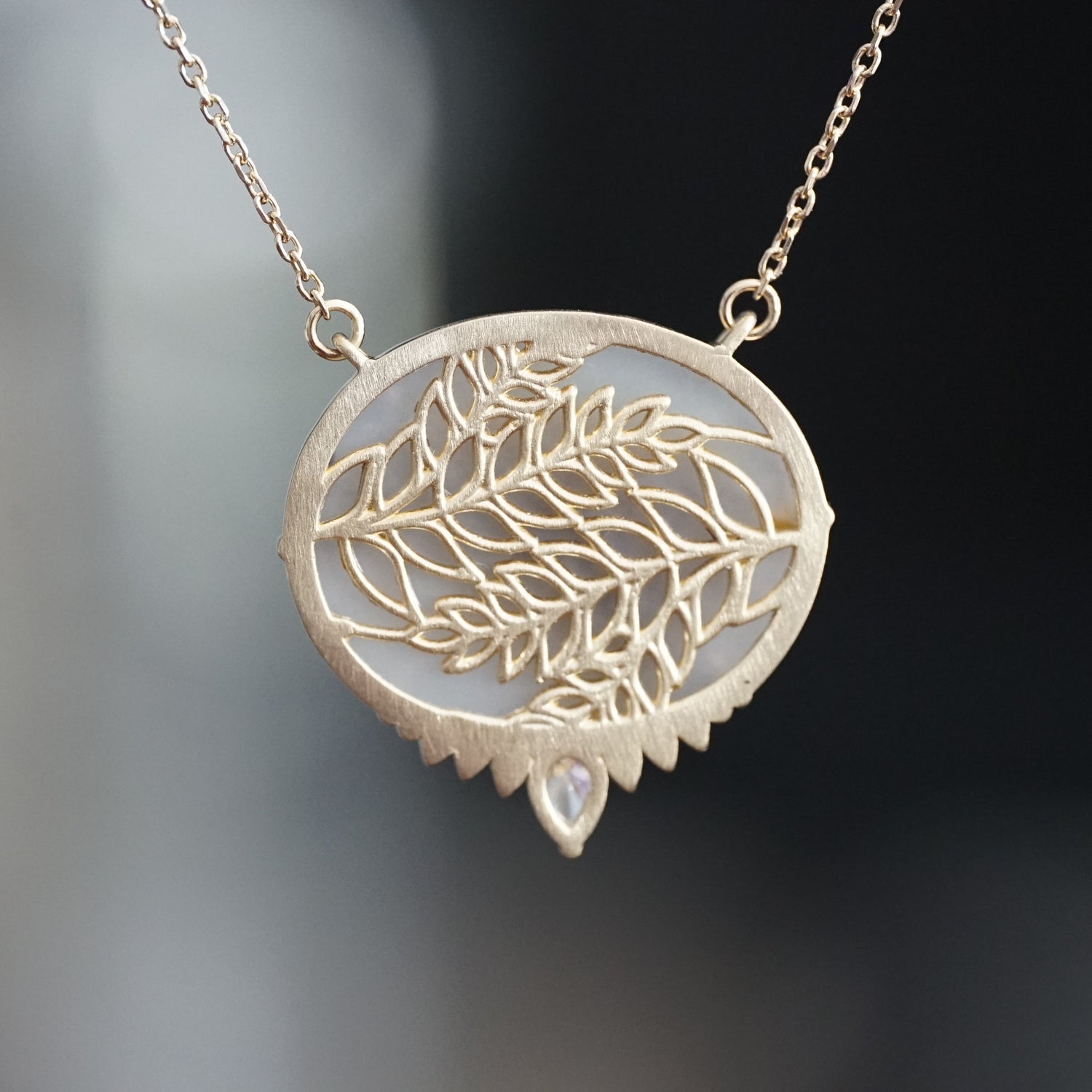 a yellow gold necklace featuring an oval dendritic agate center stone with a pear shape diamond at the base is rotated to show the leaf design on the backside