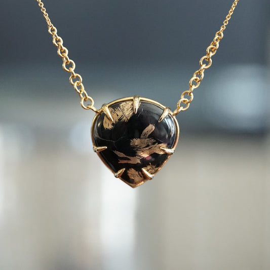 a yellow gold necklace featuring a pear shape black jade cabochon with 24K yellow gold plating on the stones natural inclusions hangs on an open link chain with tapered links