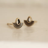 a macro photo of a yellow gold stud earring with an open pear shape and solid fan shape underneath on a glossy white background