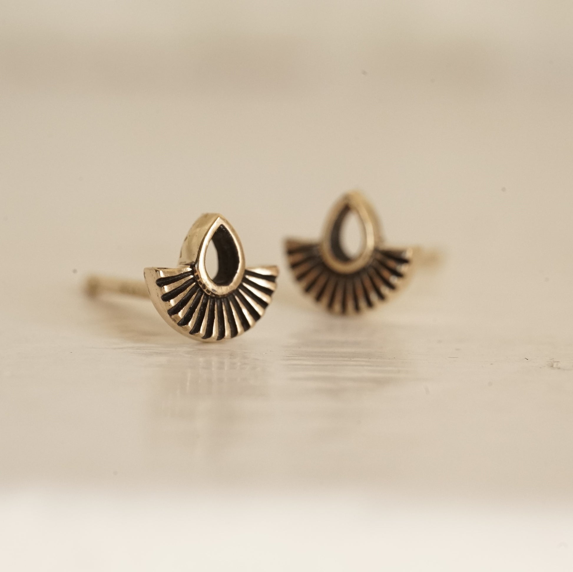 a macro photo of a yellow gold stud earring with an open pear shape and solid fan shape underneath on a glossy white background