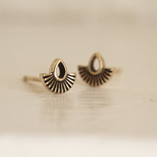 a macro photo of a yellow gold stud earring with an open pear shape and solid fan shape underneath on a glossy white background