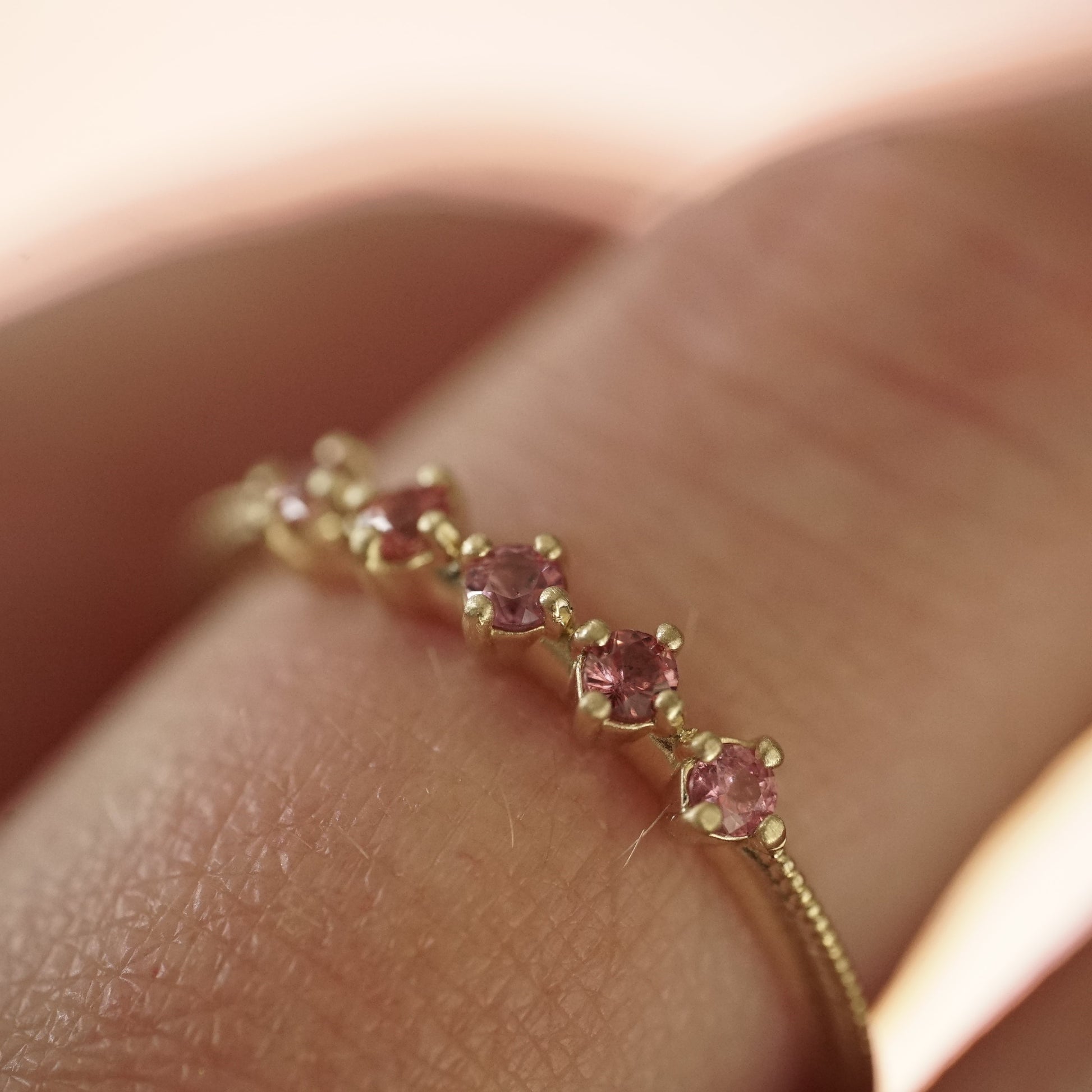 a macro photo of a yellow gold band with 5 prong set pink padparadscha sapphires on a light skinned left hand