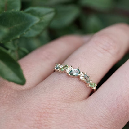 a yellow gold ring features green and teal gemstones paired with round white diamonds in a playful design on a light skinned left hand