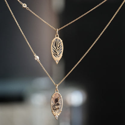 a pair of a yellow gold pendants featuring an oval dendritic agate and one pear shape diamond hang on chains which each feature one rose cut diamond, one pendant has been rotated to show the detail leaf design on the back.