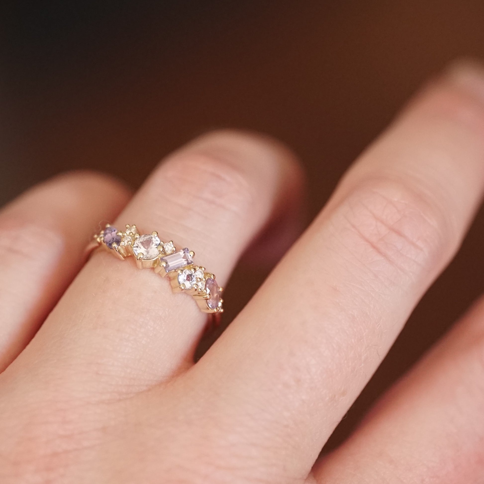 a yellow gold ring featuring purple and blue sapphires of mixed shapes and sizes are paired with round diamonds in a playful design on a light skinned left hand