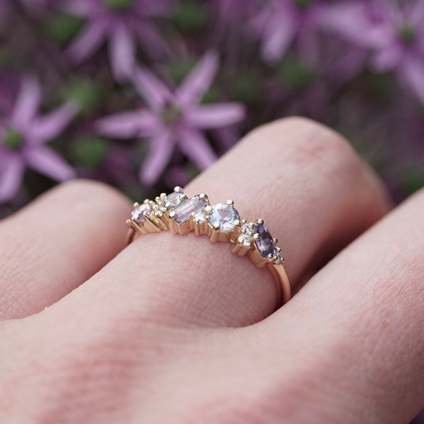 a yellow gold ring featuring purple and blue sapphires of mixed shapes and sizes are paired with round diamonds in a playful design on a light skinned left hand