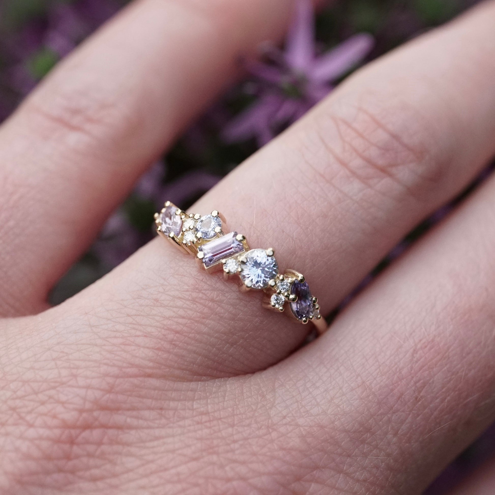 a yellow gold ring featuring purple and blue sapphires of mixed shapes and sizes are paired with round diamonds in a playful design on a light skinned left hand