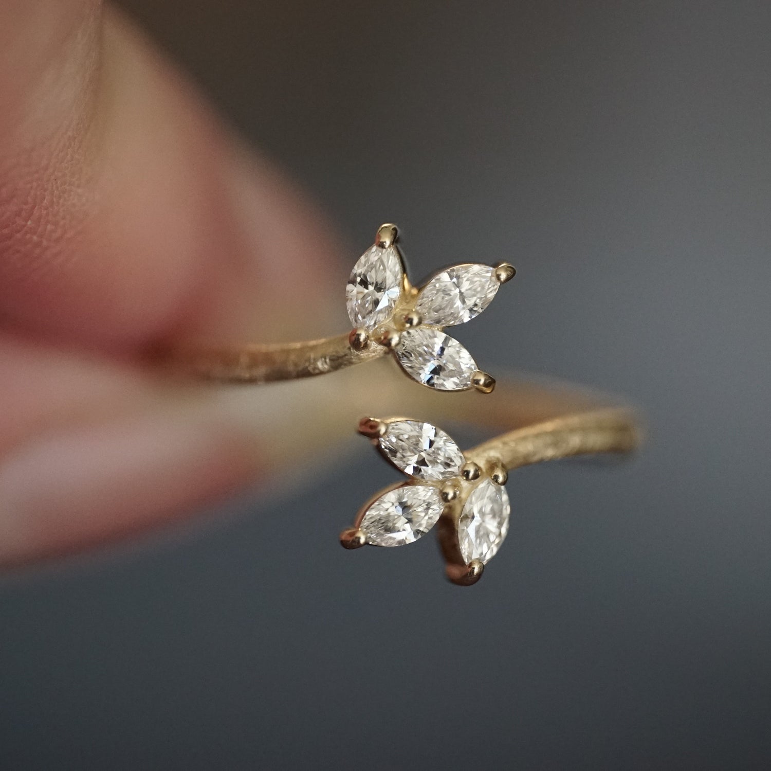 a macro photo of a yellow gold and diamond leaf inspired stacking ring held between fingers